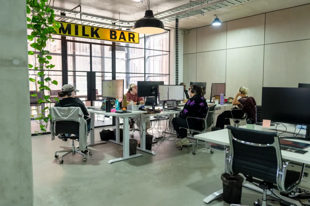 Open-plan desks under a Milk Bar signage and trailing plants, Clinibase office fitout, Collingwood.